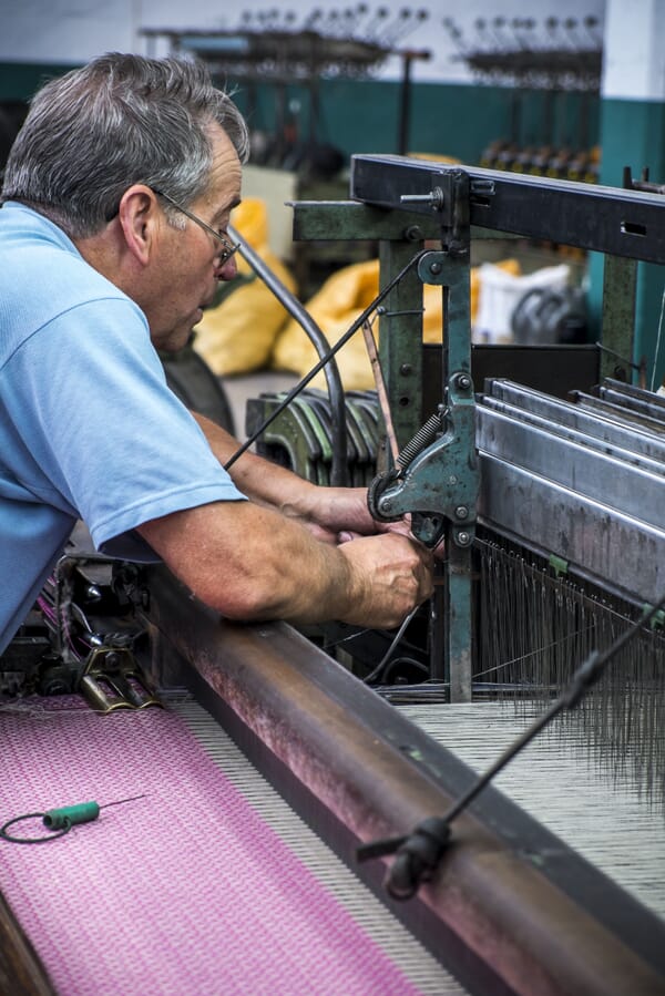 Weaver working at a loom with pink wool cloth in a mill in Portugal