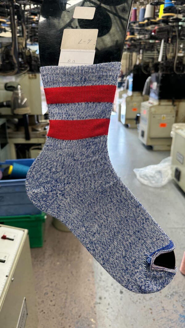 Hand holding a freshly knitted striped sock beside the knitting machines