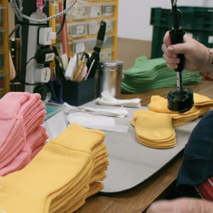 Hands pressing finished socks with stacks of pink and yellow socks on the table