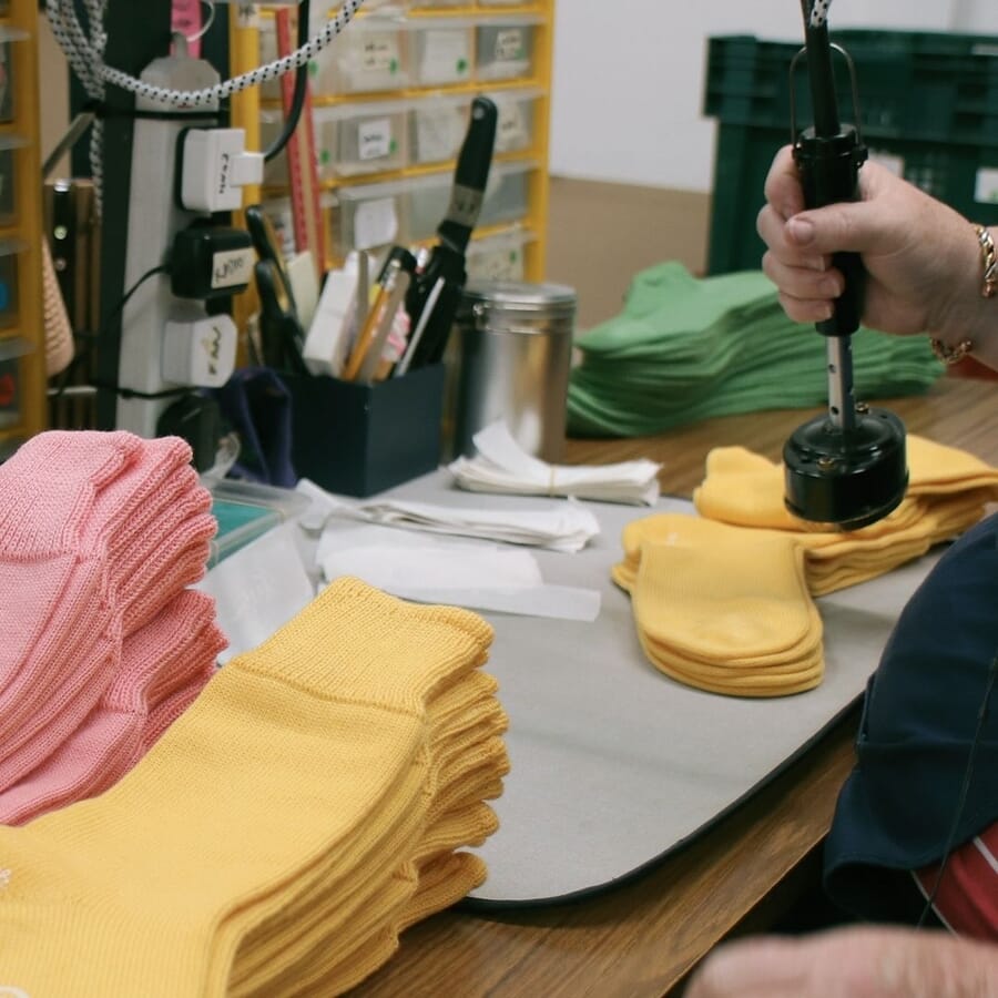 Hands pressing finished socks with stacks of pink and yellow socks on the table