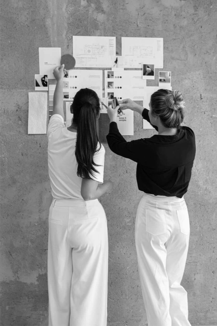 Black and white photo of two designers pinning sketches to a wall board