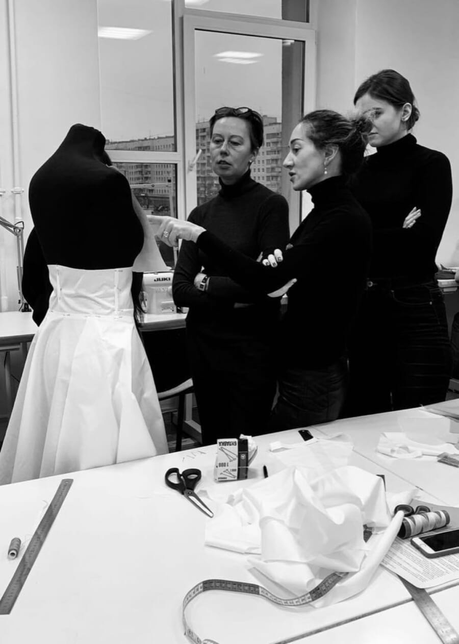 Black and white photo of a team gathered around a white dress on a dress form