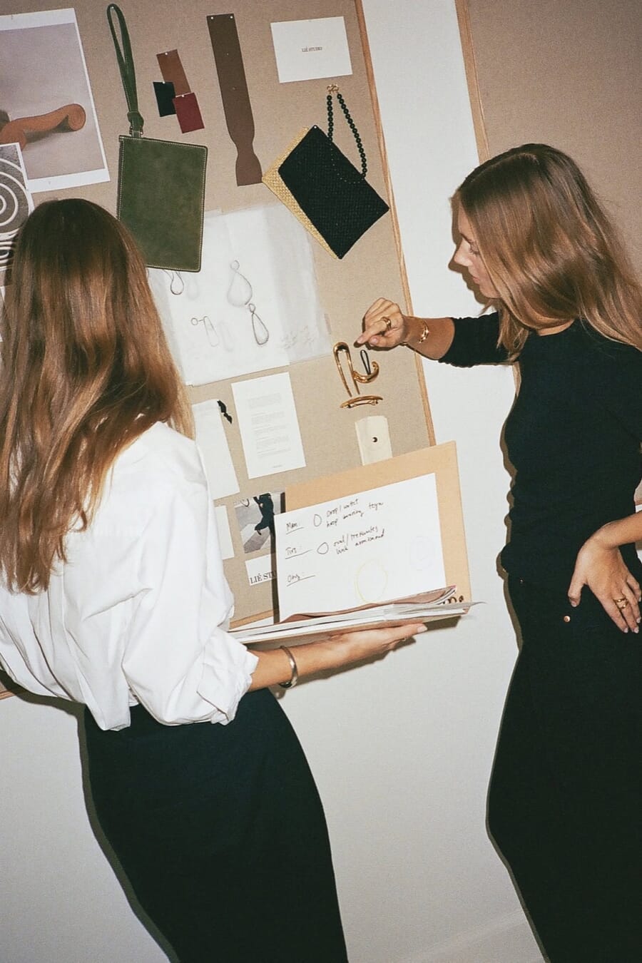 Two designers pinning fabric swatches and sketches to a wall board