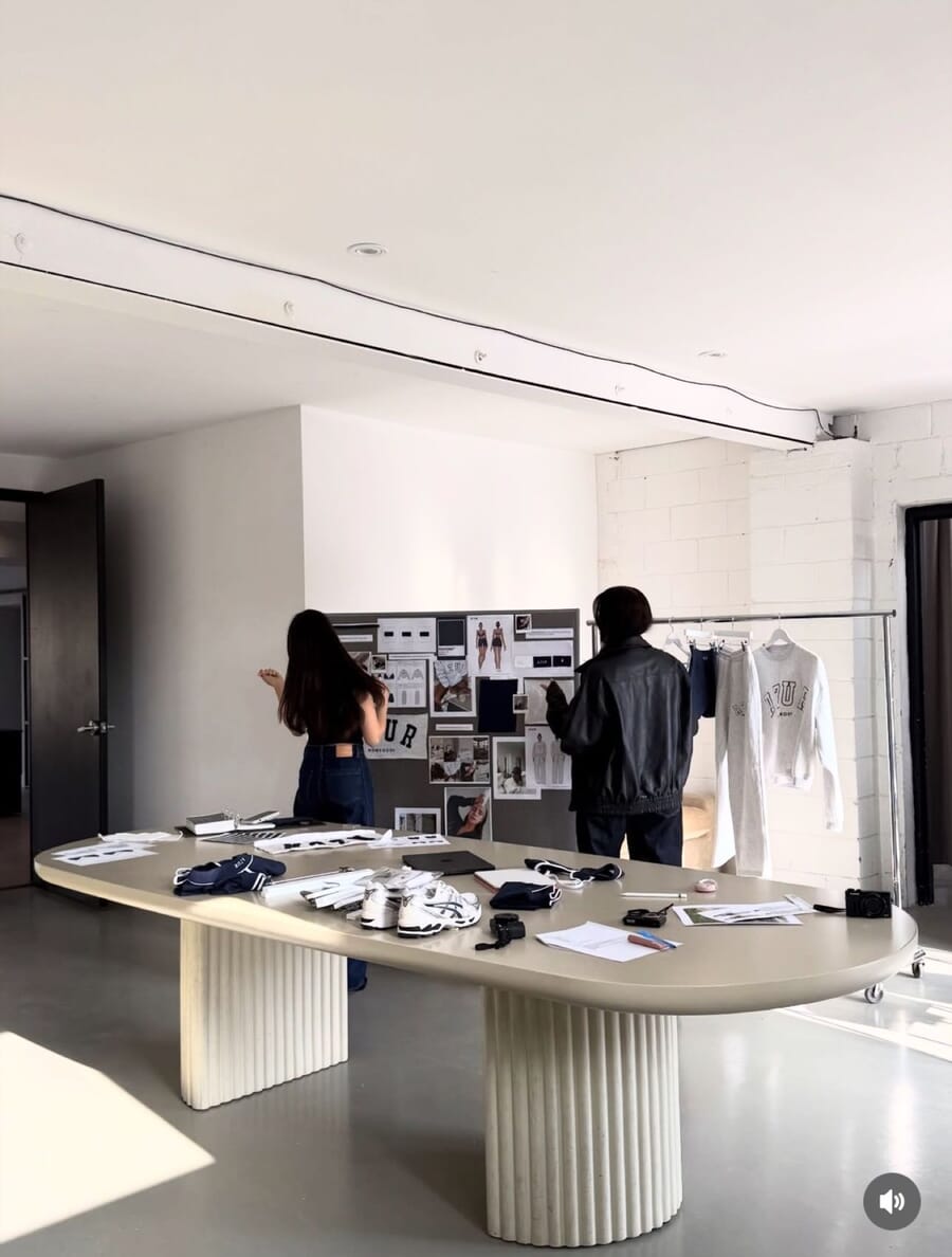 Quiet studio with a long oval table, moodboards on the wall and a garment rail