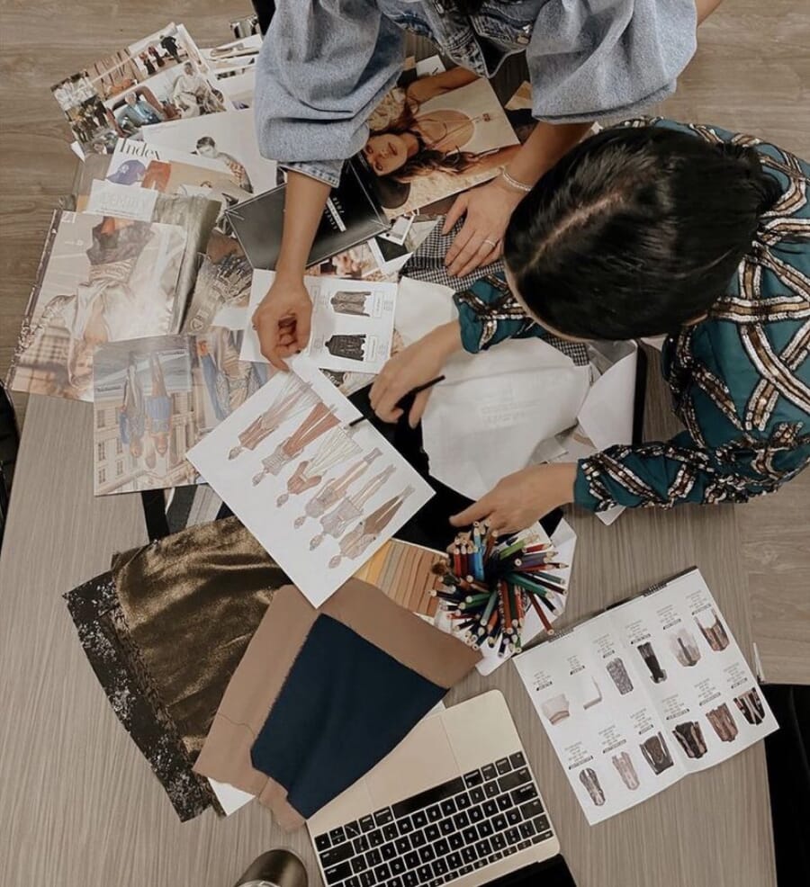 Overhead view of hands sorting printed sketches, fabric swatches and reference photos on a table