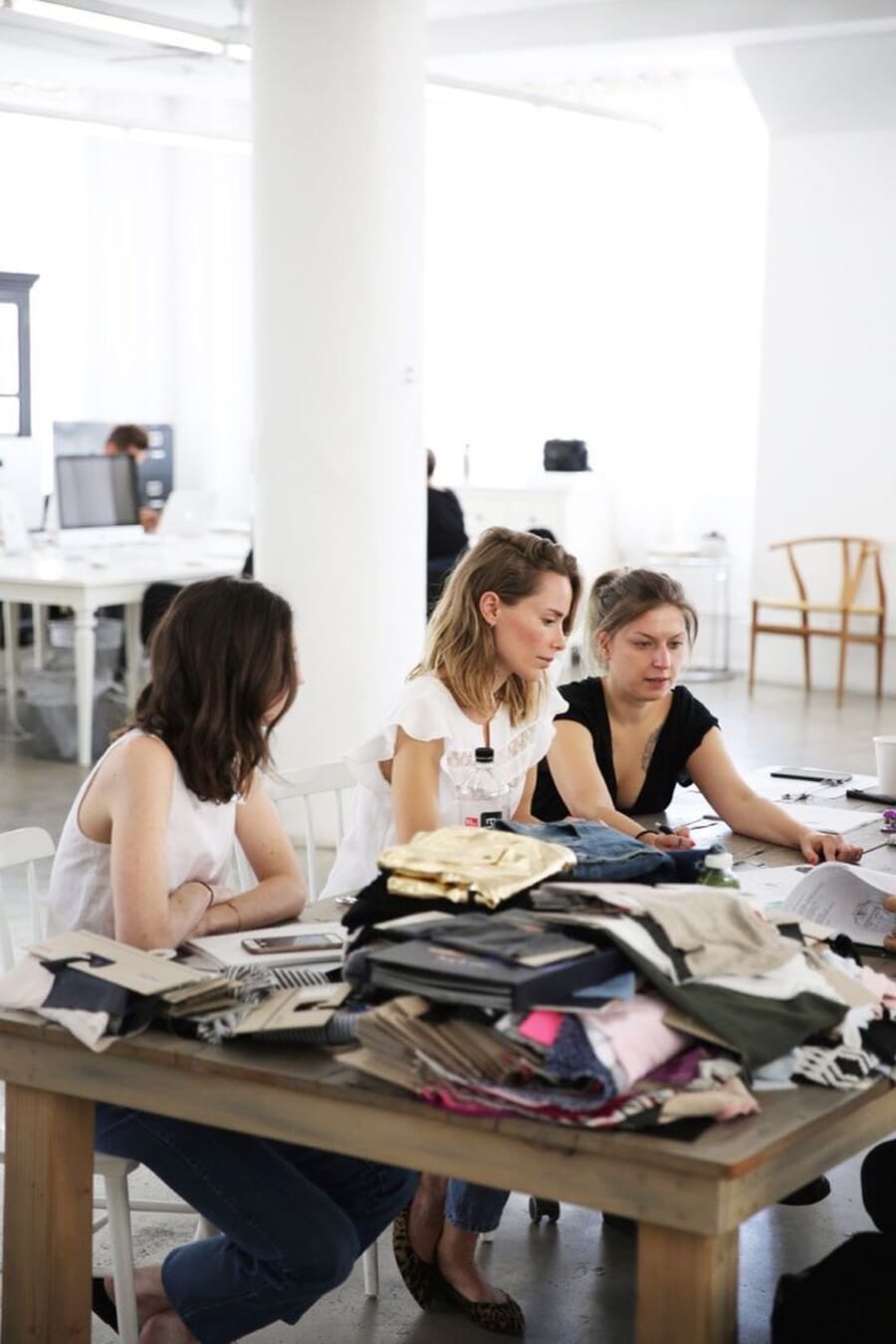 Three designers at a table covered with fabric samples and laptops