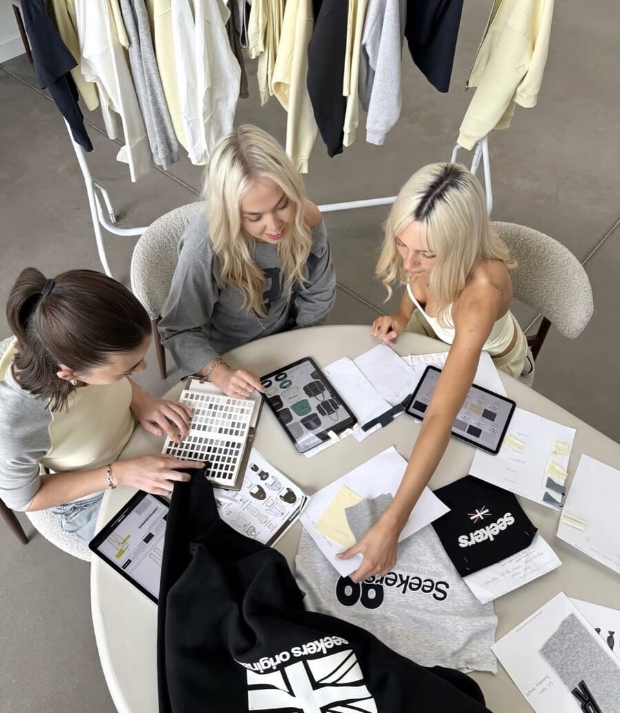 Overhead view of designers at a round table with printed flats and a sweatshirt sample