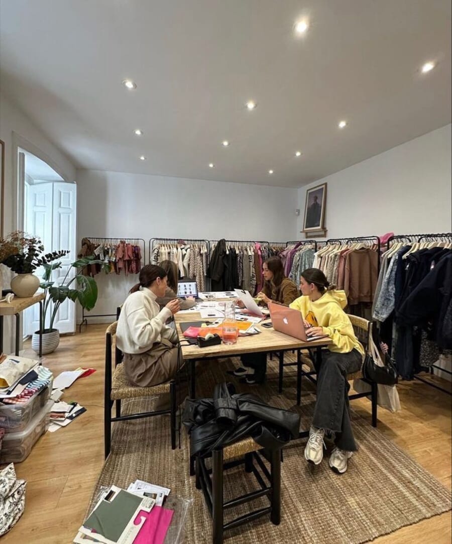Bright studio with a long work table and rails of clothing along the walls