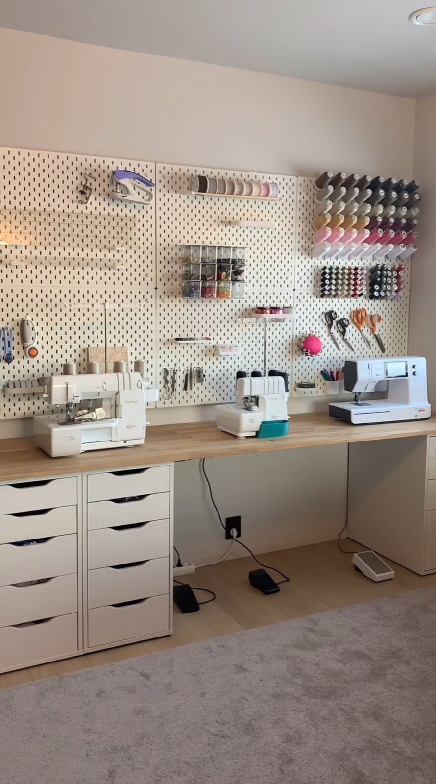 Sewing corner with machines on a white desk and thread spools on a pegboard