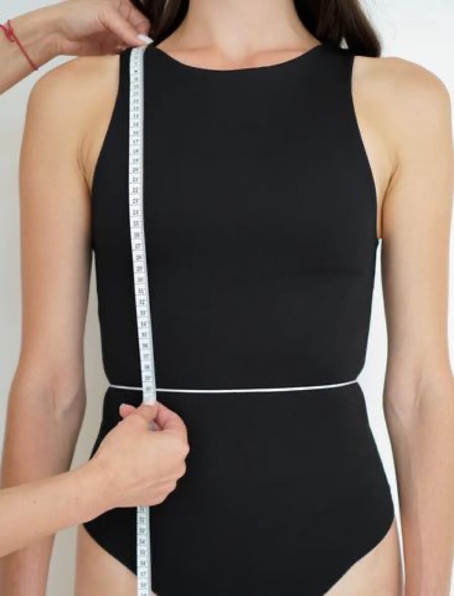 Measuring a black bodysuit at the waist with a tape measure