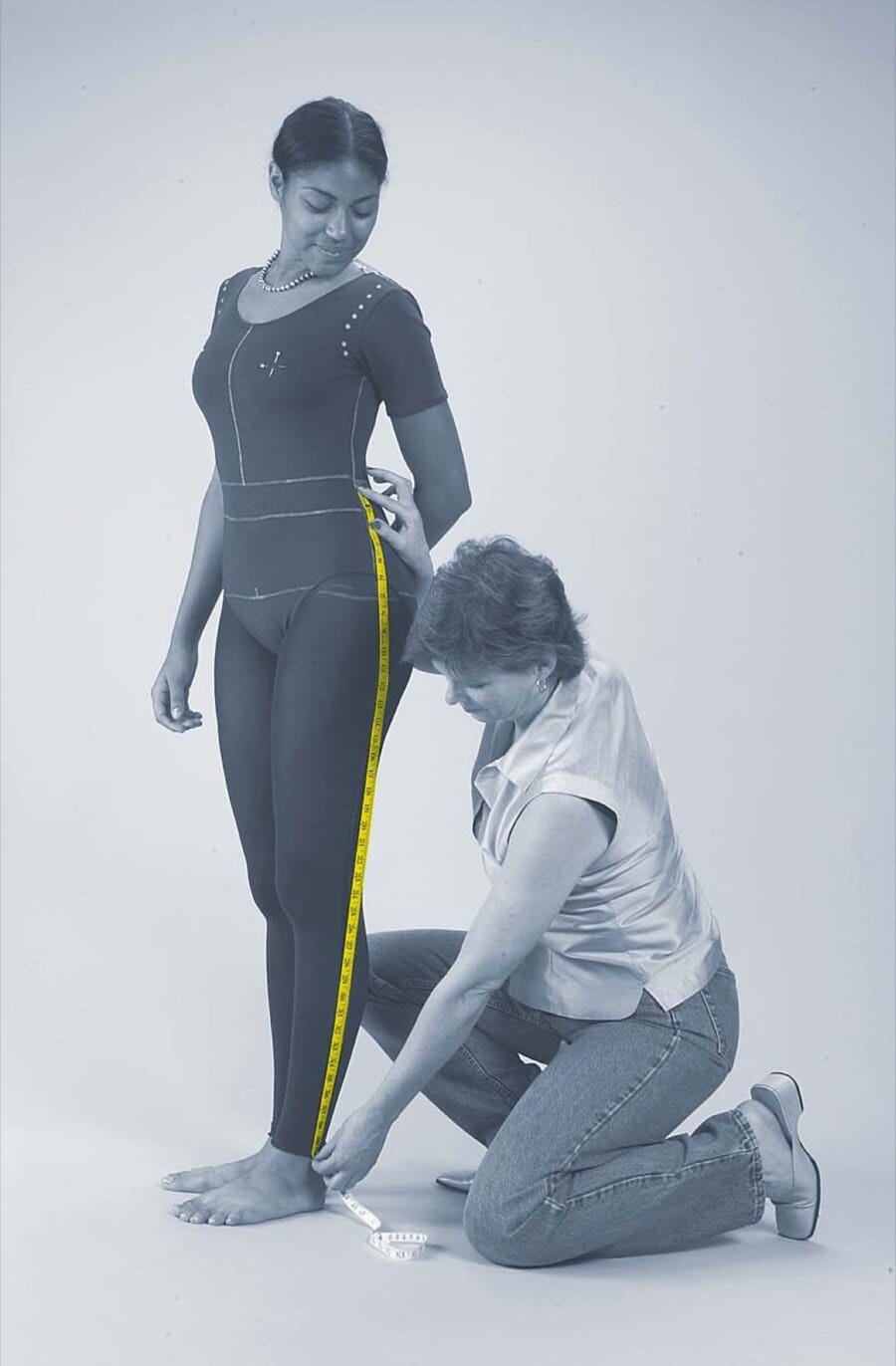 Technical designer kneeling to measure the inseam of a fit model with a tape measure