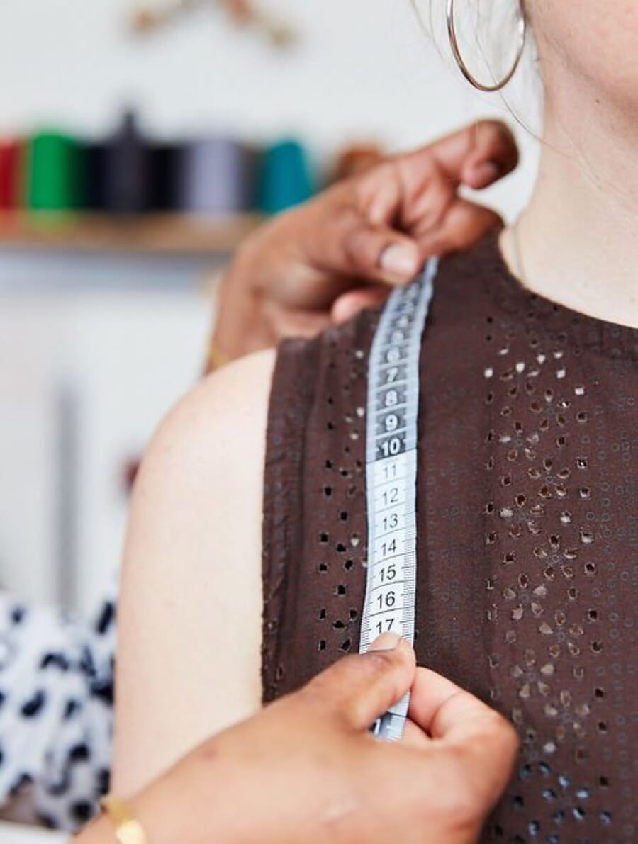 Hands holding a tape measure at the shoulder seam of a brown knit top