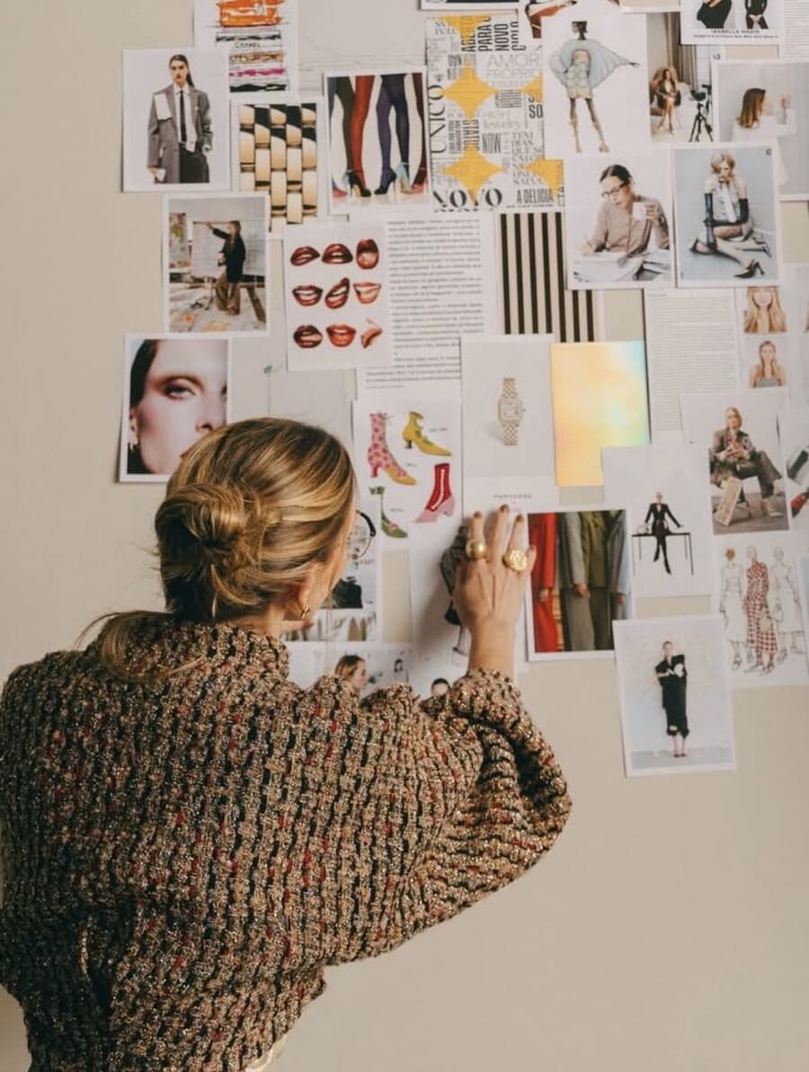 Designer pinning reference images to a wall covered in photos
