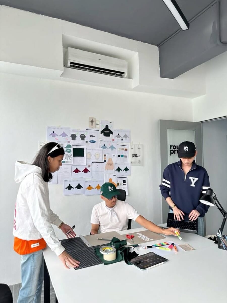 Team at a white table reviewing flat sketches and color swatches, with flats pinned on the wall