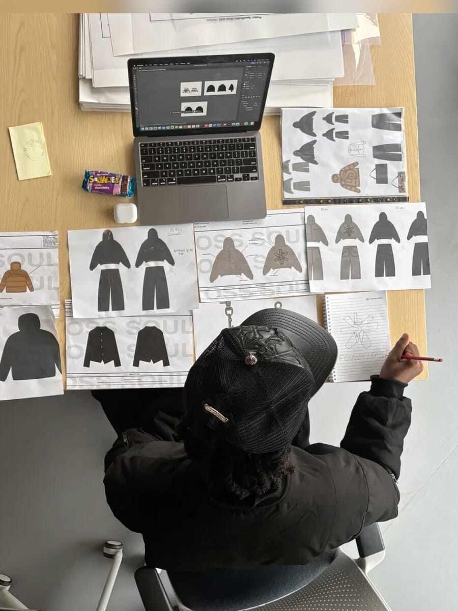 Designer drawing garment flats next to a laptop and printed sketches
