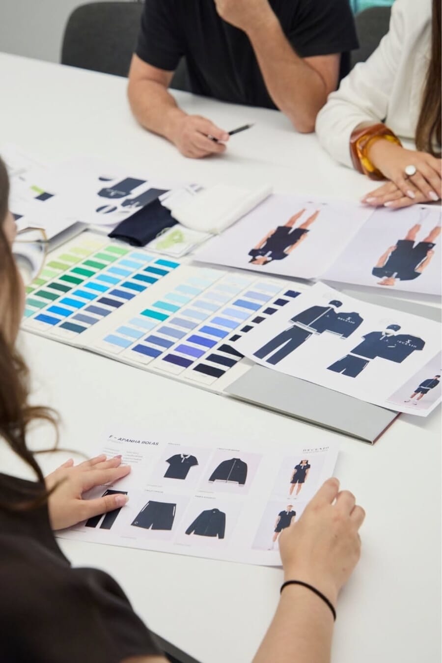 Hands pointing at printed flat sketches and color swatch strips on a white table