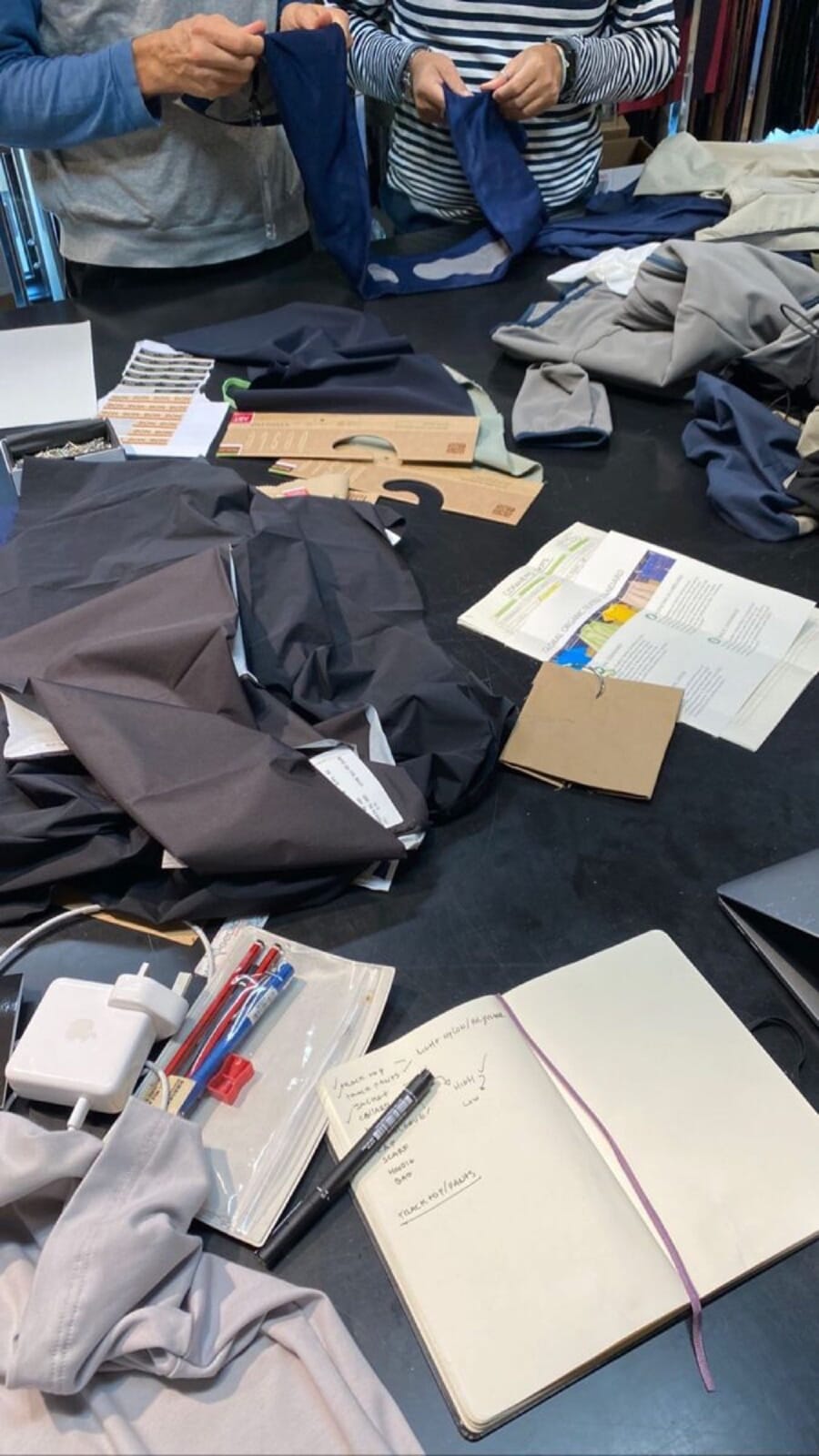 Overhead view of fabric pieces, notebooks and pens on a work table