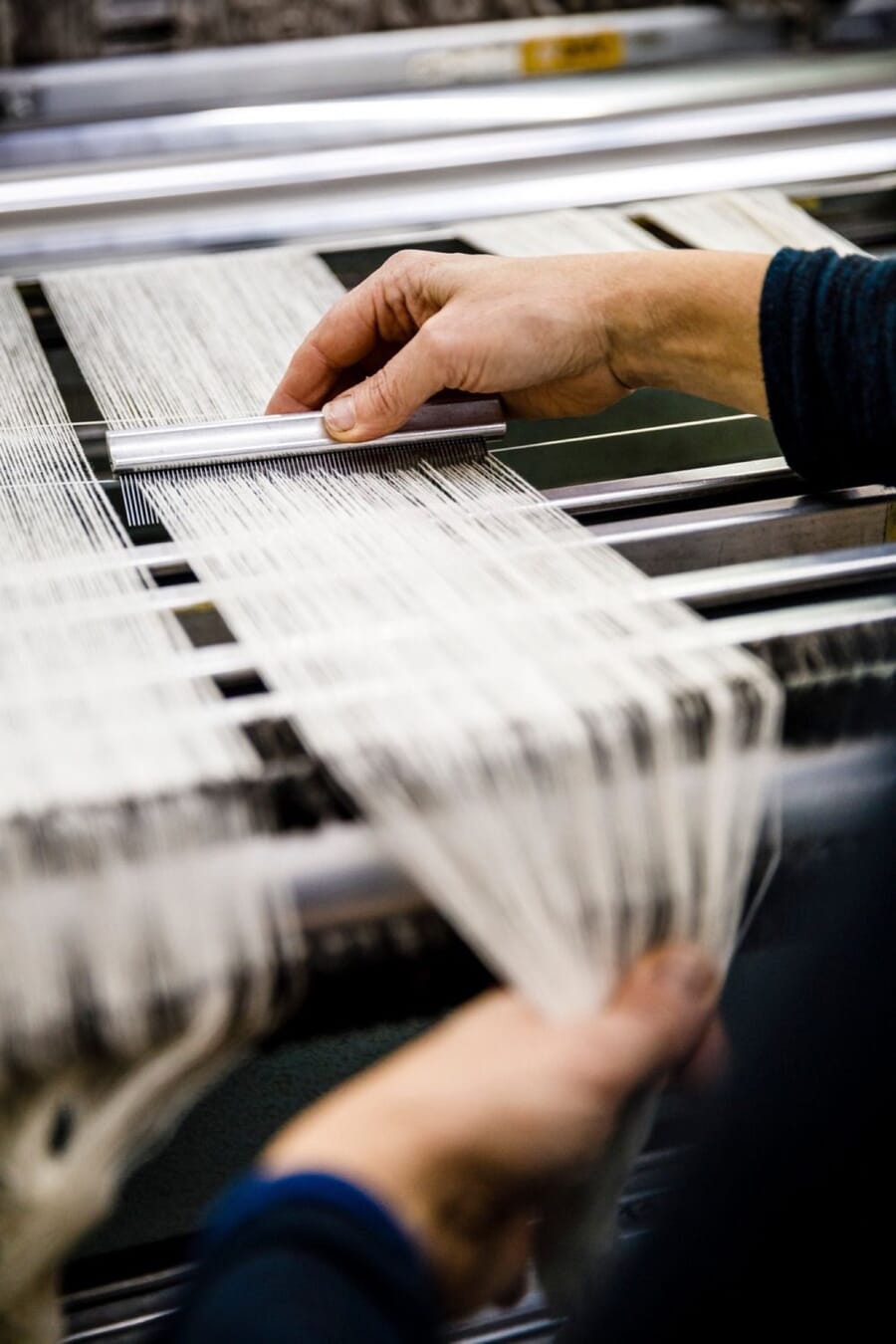 Hands drawing white warp threads across a loom