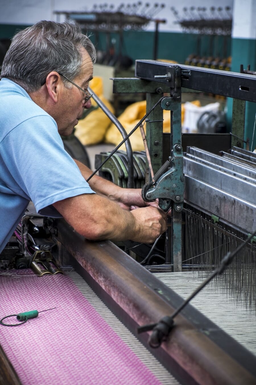 T&eacute;cnico a afinar um tear com tecido rosa