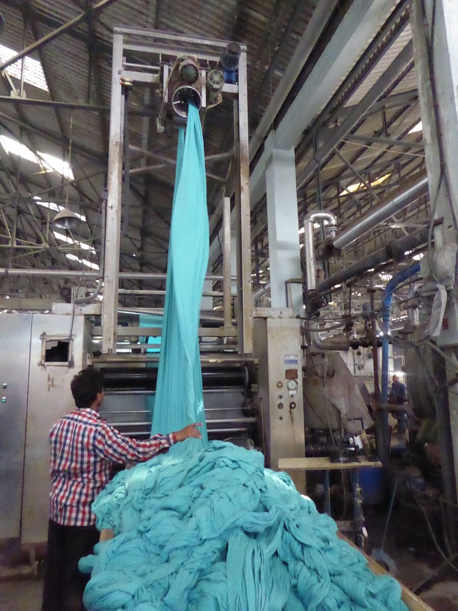 Worker guiding teal dyed fabric out of a dyeing machine into a heap