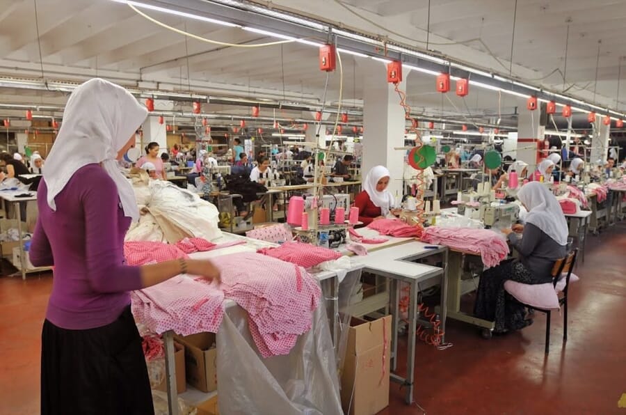 Operator sorting pink knit garments at a sewing table on a long, busy sewing floor