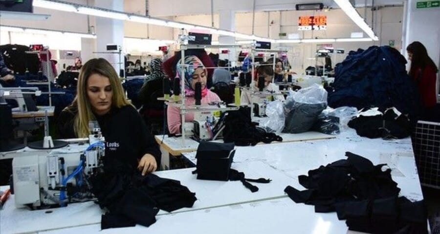 Machinist with piles of cut black garment pieces on a white work table