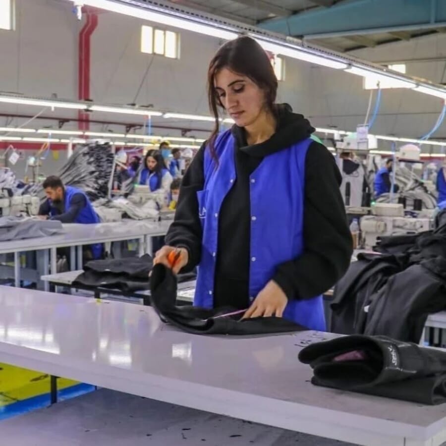 Worker in a blue vest trimming loose threads from a black hoodie at a white table
