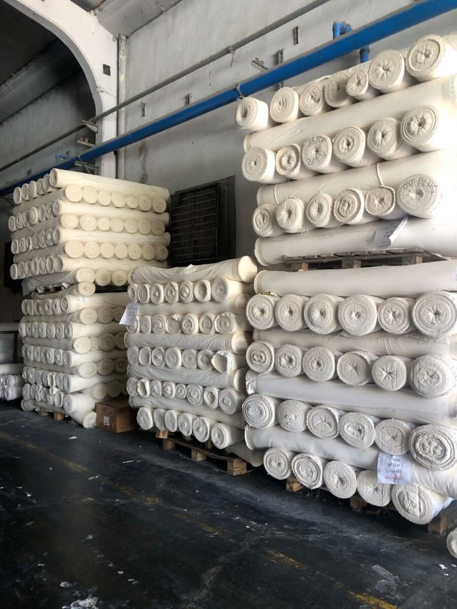 Pallets of white, unfinished fabric rolls stacked in a warehouse