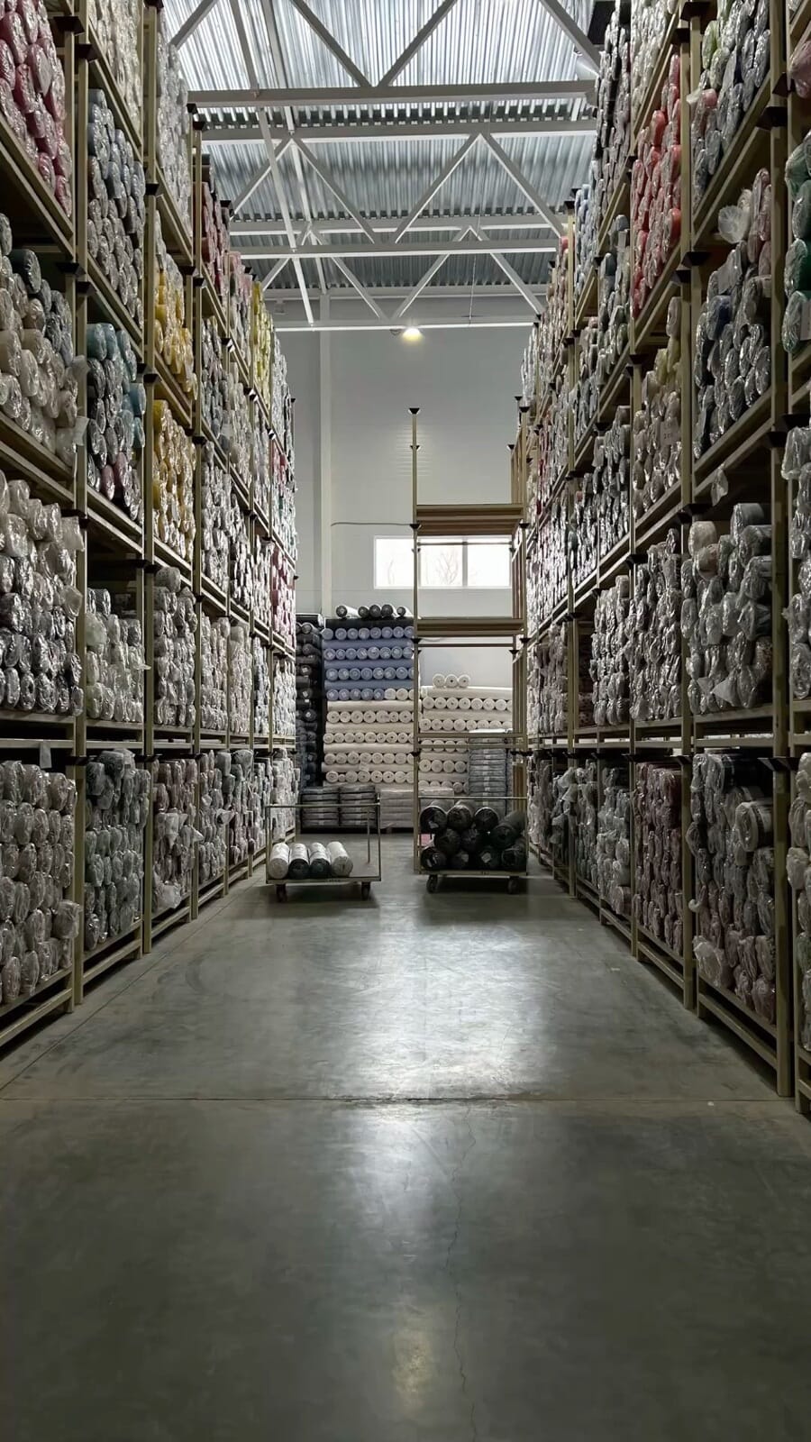 Tall racks of fabric rolls on both sides of a warehouse aisle