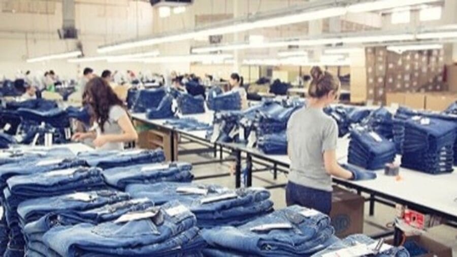 Workers folding and stacking finished jeans on long tables