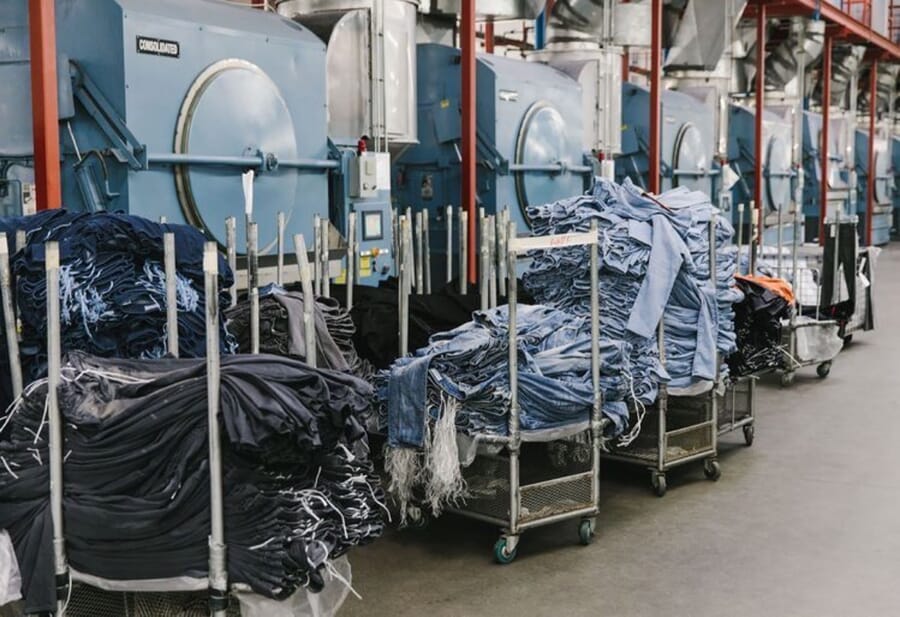 Carts loaded with washed jeans in front of a row of industrial washing machines