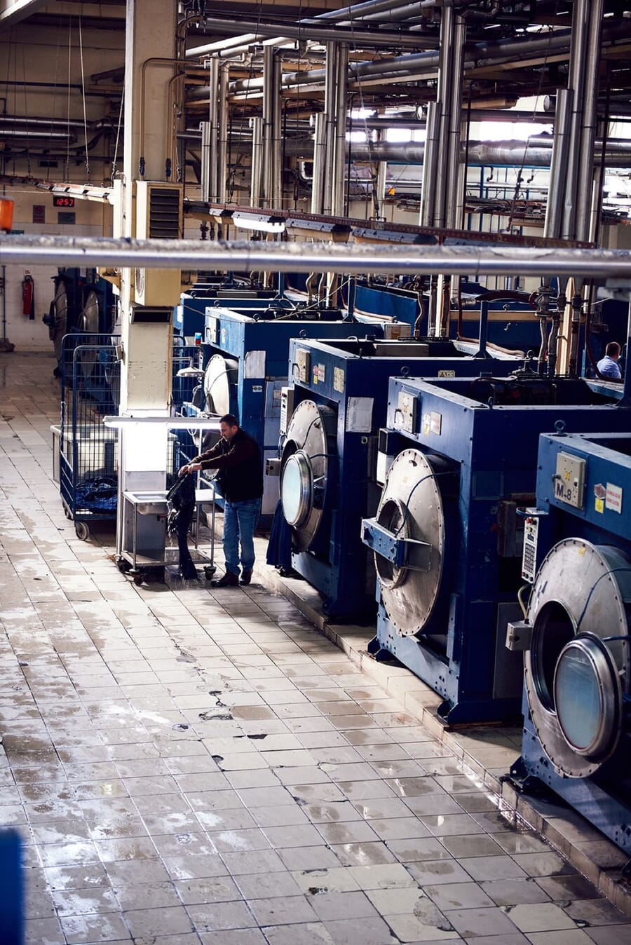 Line of blue industrial garment washing machines along a wet laundry floor