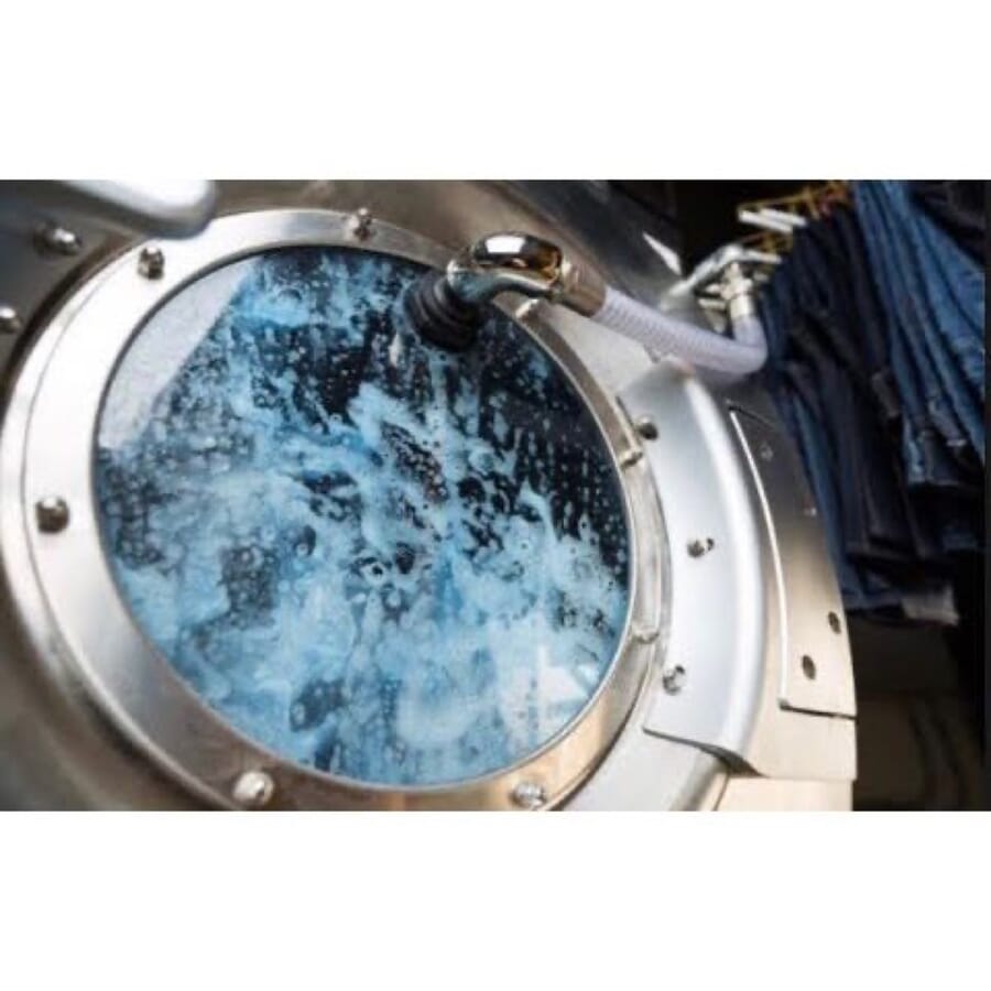 Porthole of an industrial washing machine with water and indigo garments churning inside