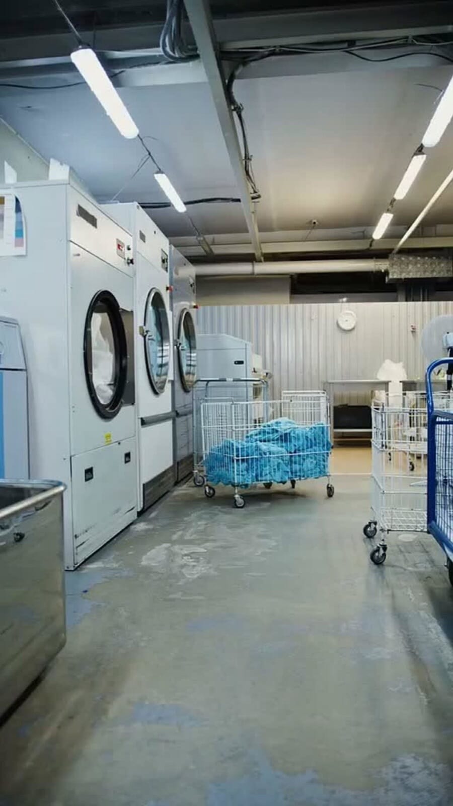 Laundry hall with white industrial washers and carts of blue garments