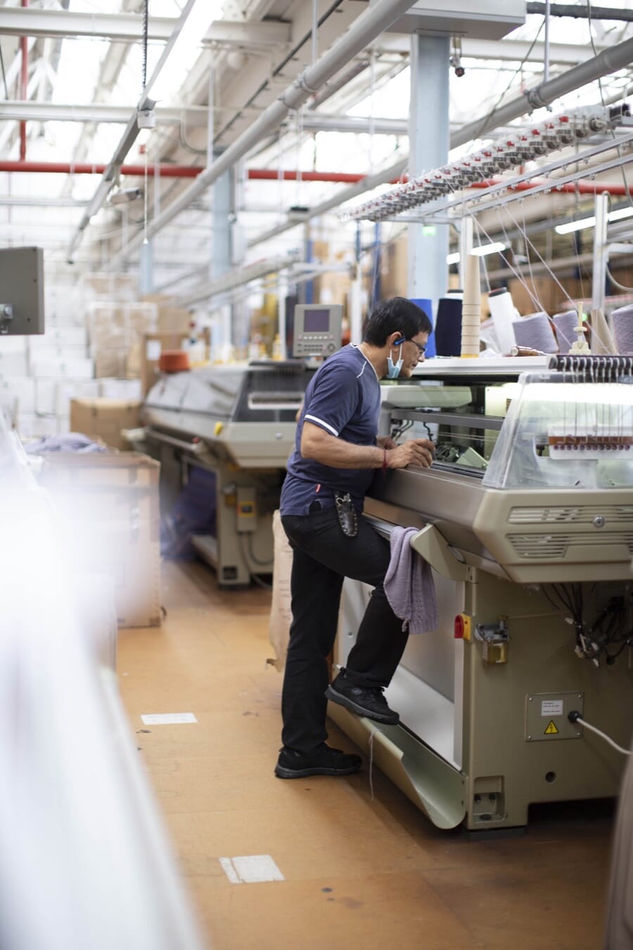 Operator checking a computerised flat knitting machine on a knitting floor