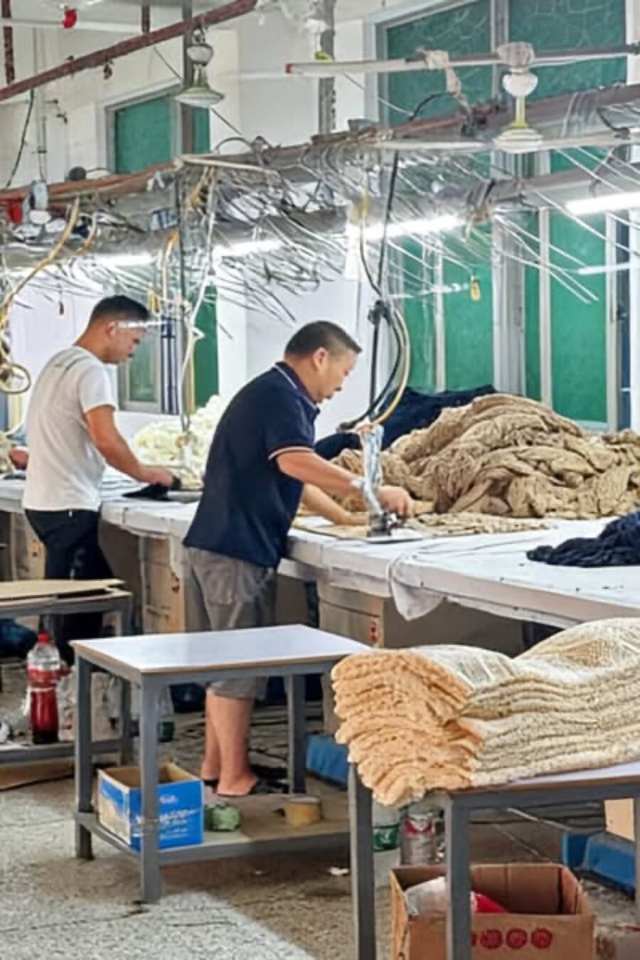 Two workers pressing and stacking beige knitwear on long tables