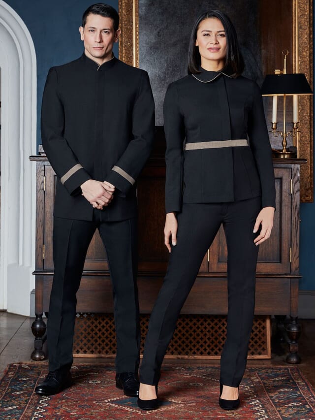 Two front-of-house staff in black tailored uniforms with beige trim, standing in a hotel lobby
