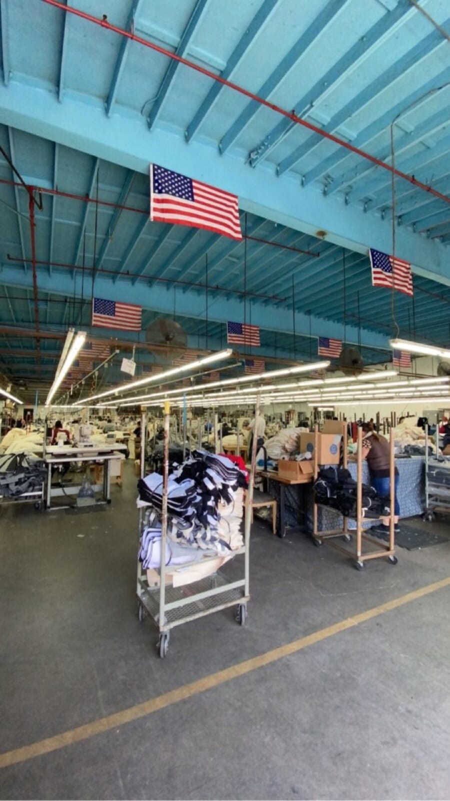 Long sewing floor with US flags hanging from the roof beams and carts of cut work in the aisle