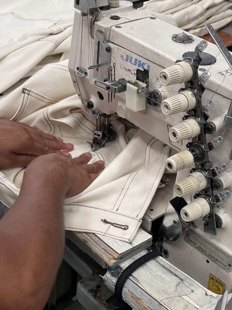 Close-up of hands guiding white knit fabric through an industrial coverstitch machine
