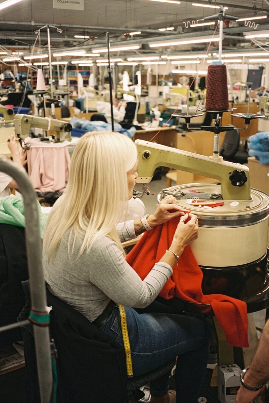 Sewing operator joining red knit panels at a machine on a busy sewing floor