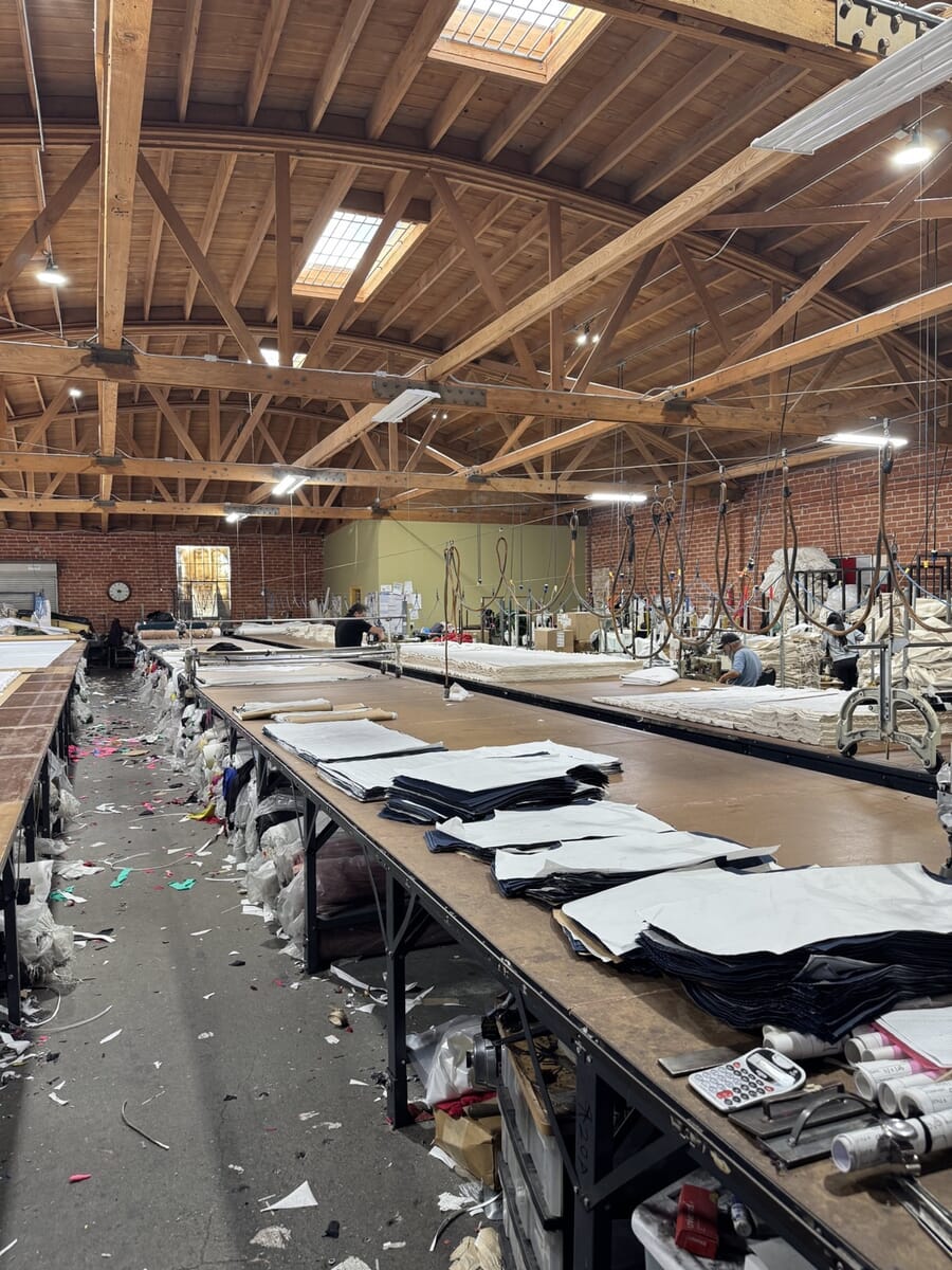 Long cutting tables under a wooden bow-truss roof with cut panels laid out in rows