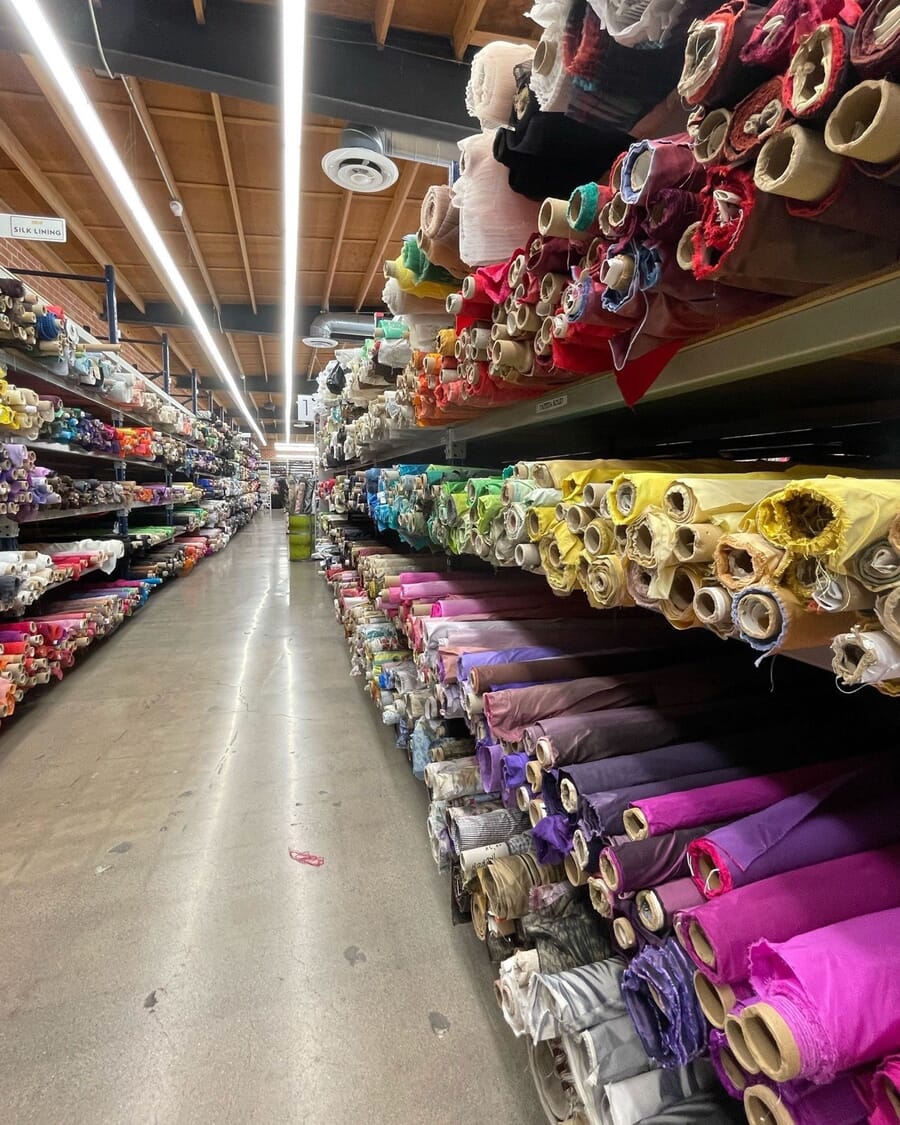Long fabric store aisle with bolts and rolls stacked to the ceiling on both sides