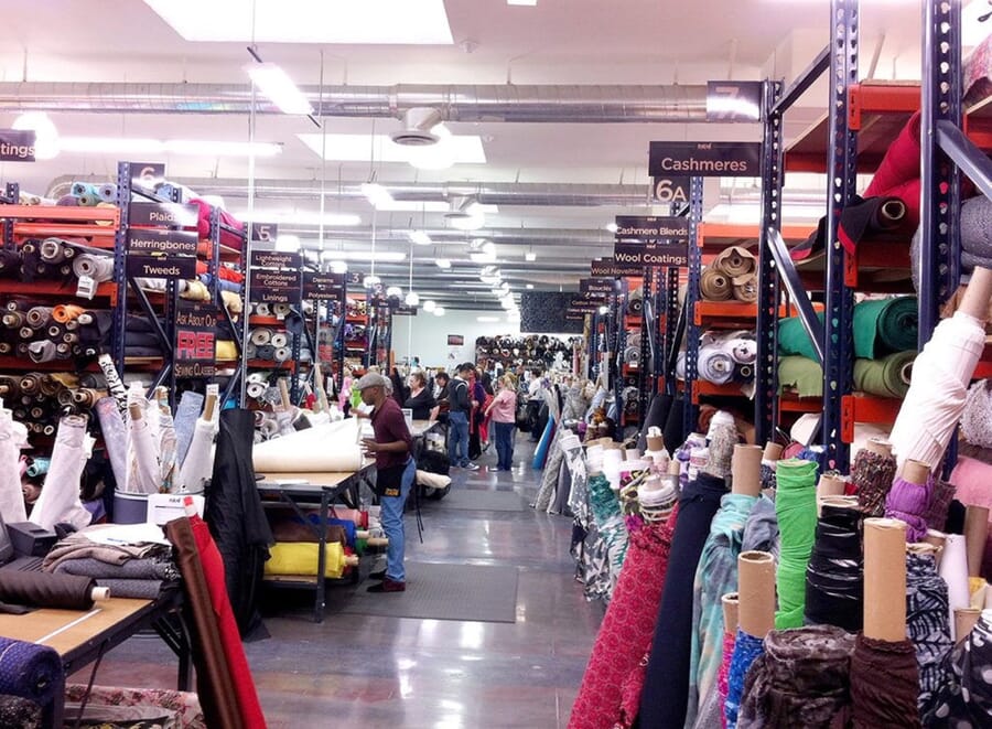 Busy fabric store with labelled shelves of wools and cashmeres and customers at the cutting counter
