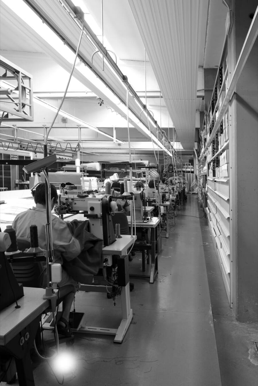 Black and white photo of a long row of sewing stations in a garment factory