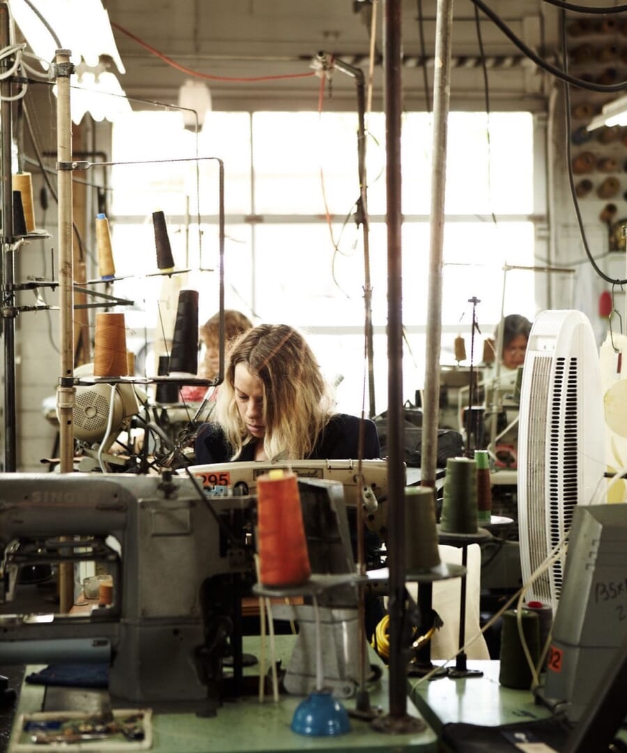 Operator at an industrial machine under tall factory windows with thread cones on the bench