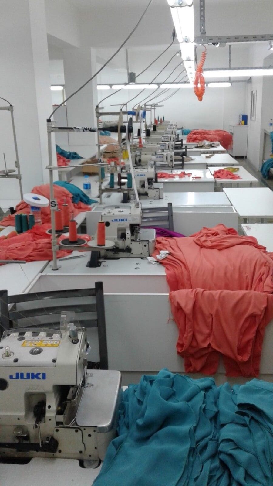 Overlock machines on a sewing line with coral and teal knit tops piled between stations