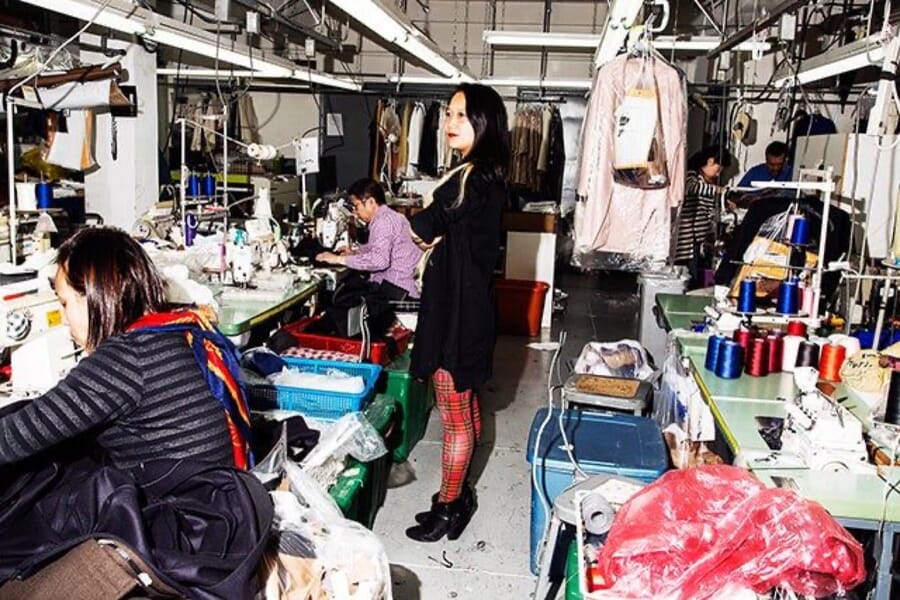 Small sample room with operators at machines and a rail of garments
