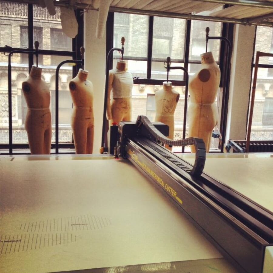 Row of dress forms by tall windows behind an automatic cutting table