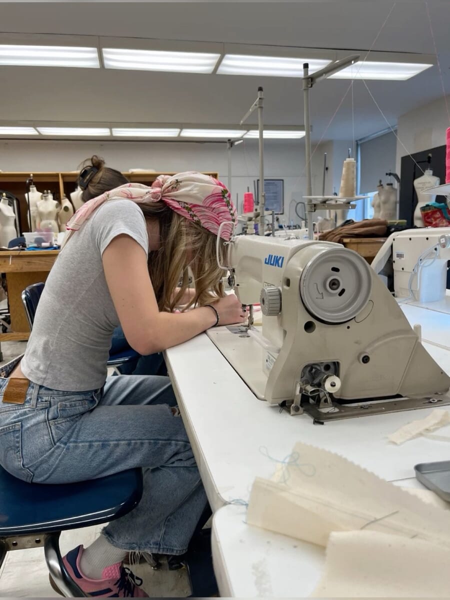 Operator leaning in to sew at an industrial machine in a sample room