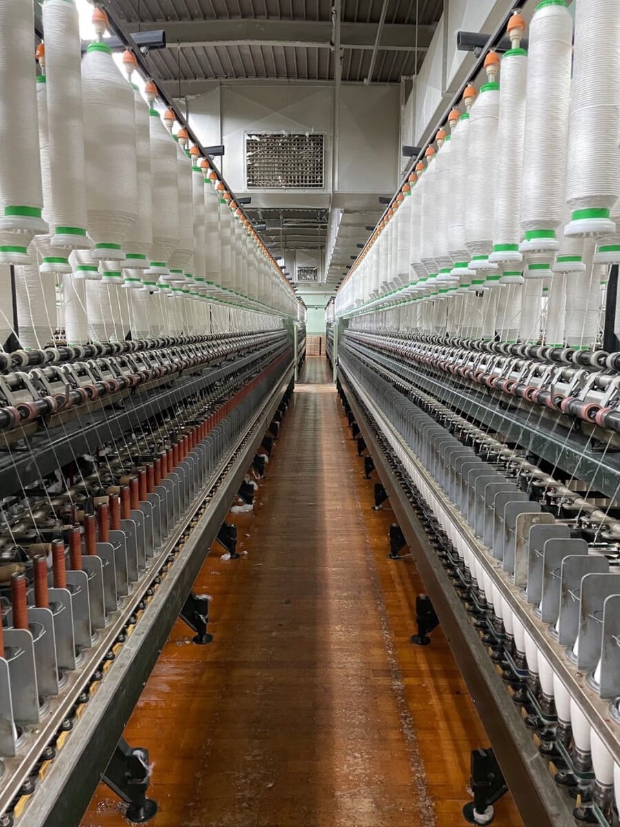 Long aisle between spinning frames loaded with white yarn bobbins in a textile mill